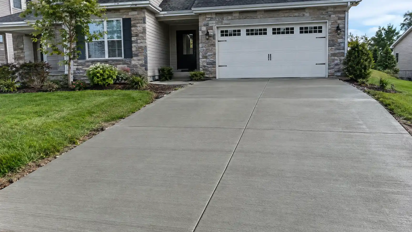 New concrete driveway leading to a two-car garage at a stone-front house