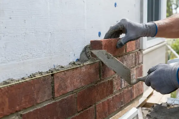 Gloved hands laying brick veneer on mortar