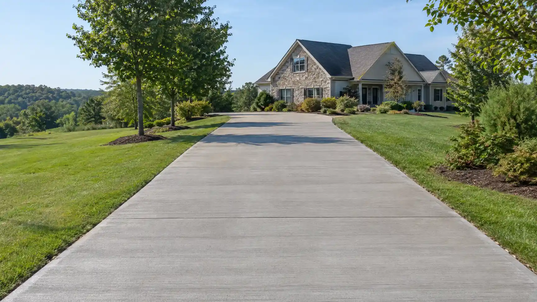 Long concrete driveway between lawns leading to a stone-front house