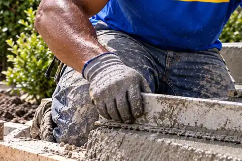 Gloved hand finishing the edge of fresh concrete beside a garden bed