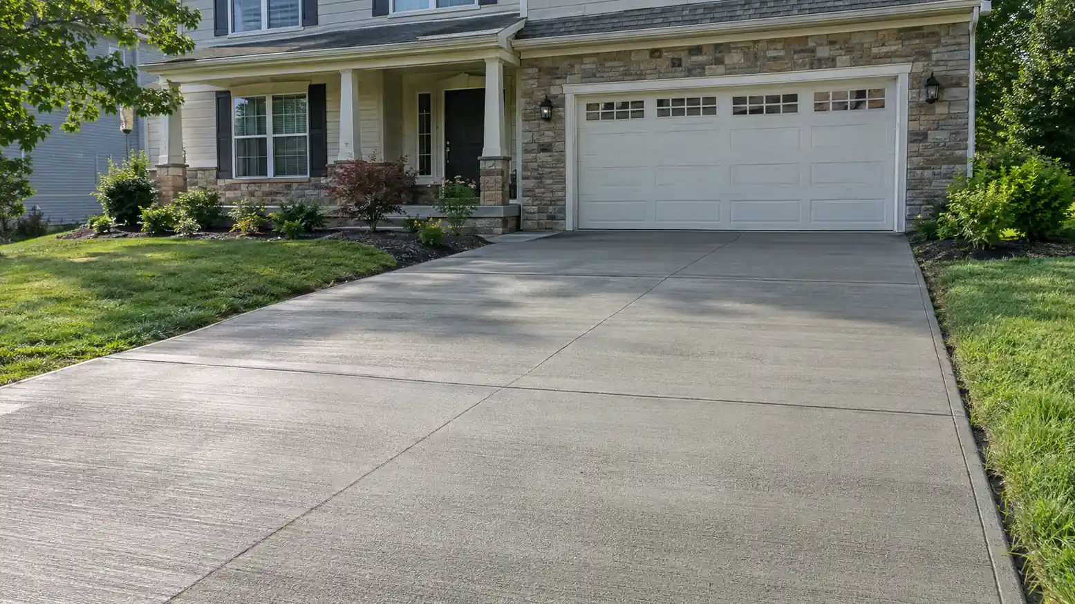 New concrete driveway in front of a stone and siding house