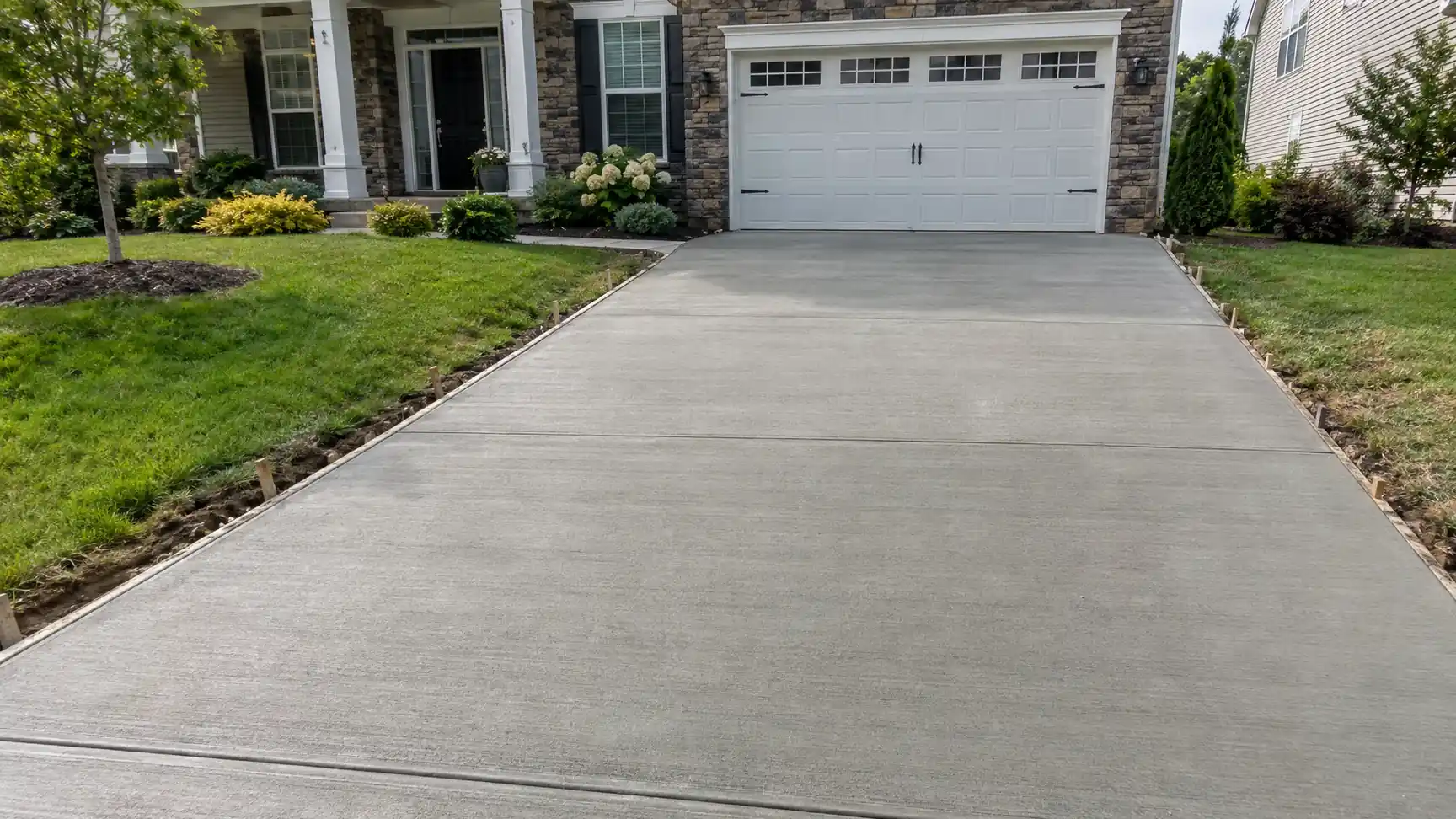 New concrete driveway between flower beds leading to a garage
