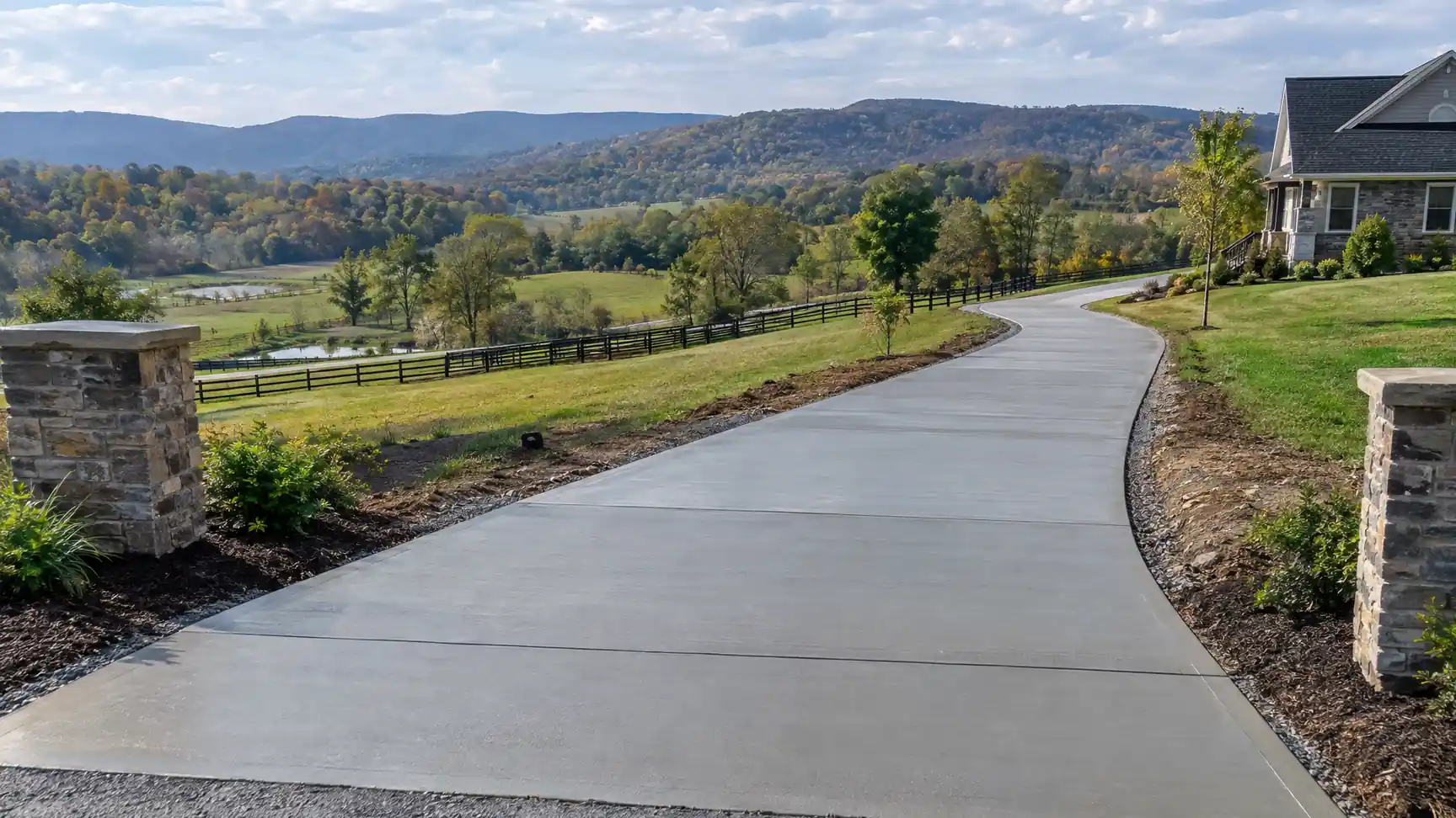 Long concrete driveway curving between stone pillars through open countryside